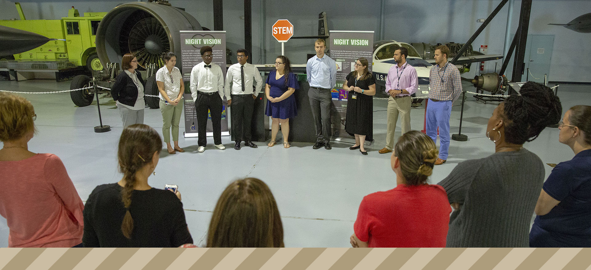 15 people of various ages and ethnicities gathered in a circle at the museum.