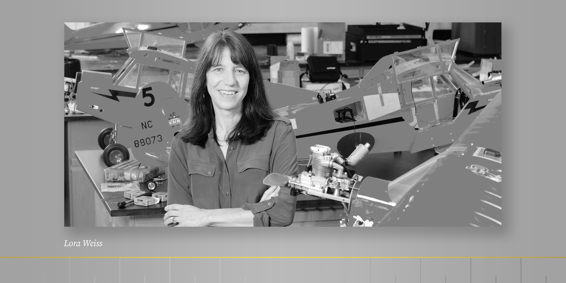 Black and white photo of woman standing in lab with model airplanes in background.