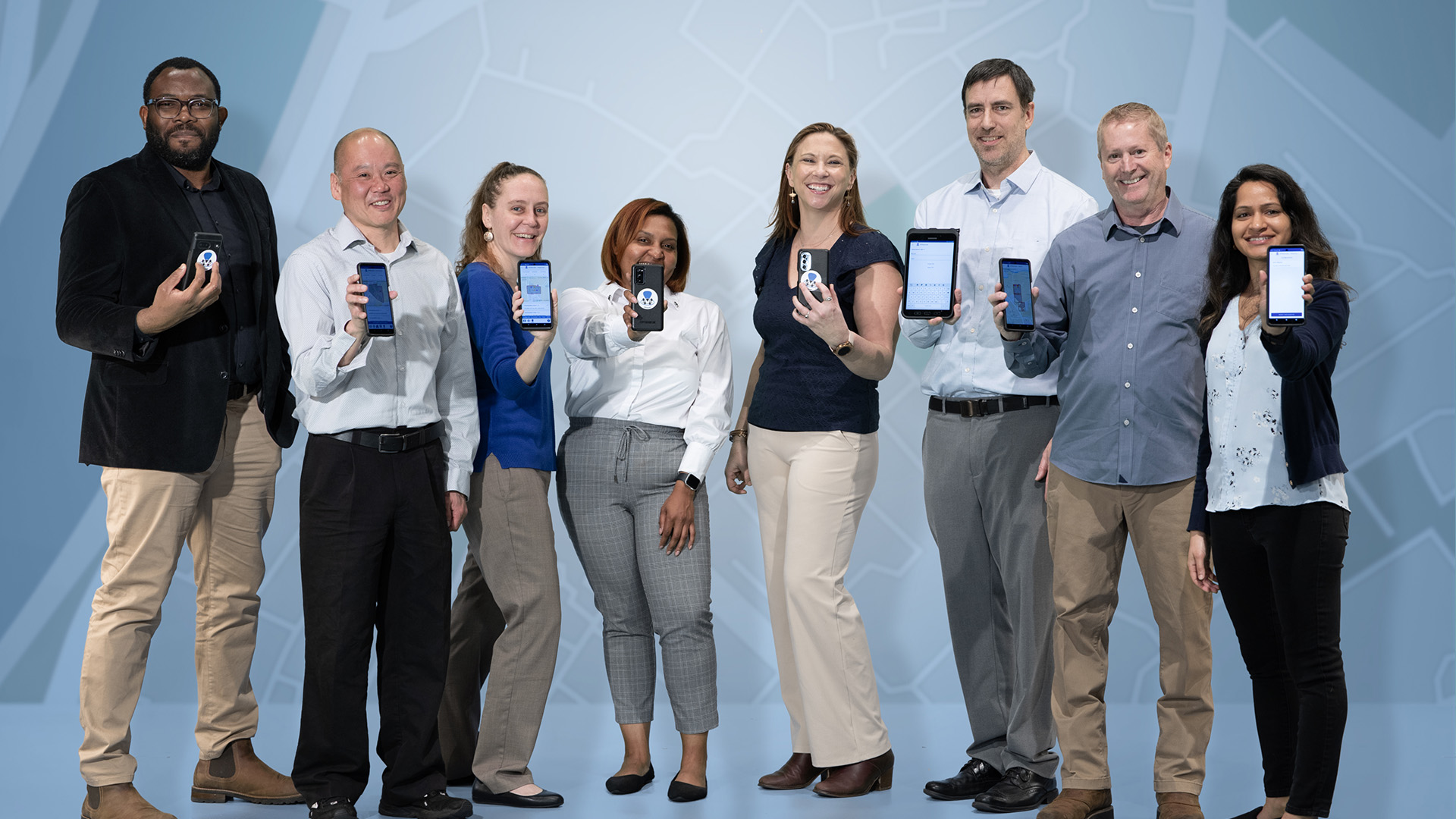 Group of eight researchers, four men and four women, dressed in street clothing, standing next to one another, holding up smartphones featuring images of app.